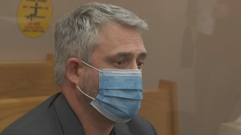 A man with grey hair and wearing a medical face mask sits in court.