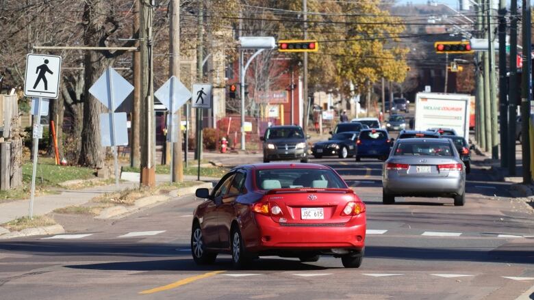 A red car turning off St. George Street with various traffic signs and lights visible in the distance.