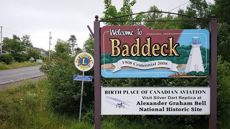 Wooden sign says welcome to Baddeck and has a picture of a lighthouse painted on it.