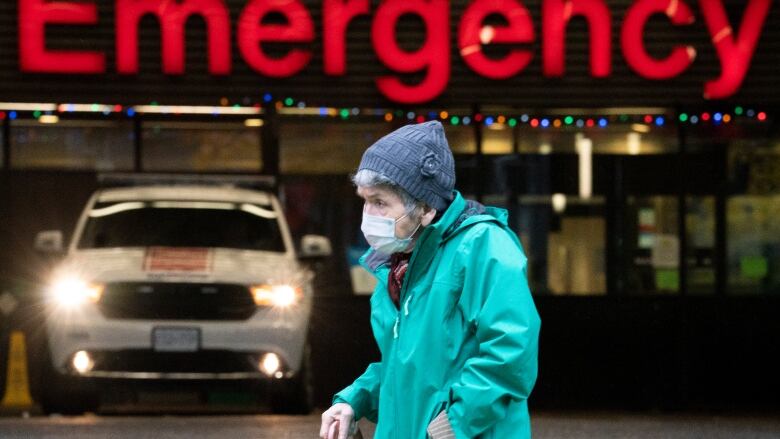 A woman wearing a mask and walking in front of an emergency sign.