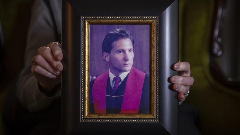 A photo frame held for the camera showing a man in graduation gown.