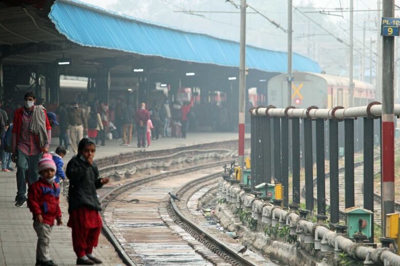 Two small children stand on a platform next to railway tracks.