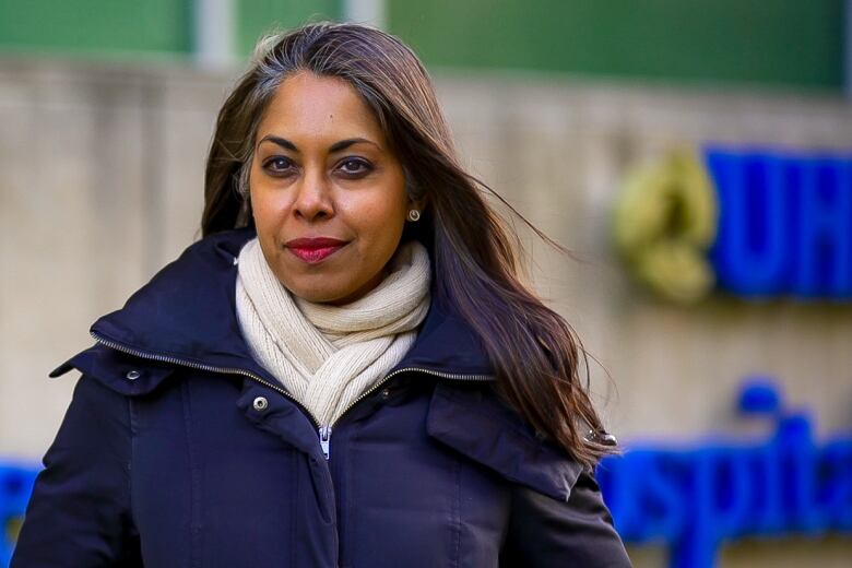 Portrait of Dr. Susy Hota, outdoors in front of a University Hospital Network sign. 