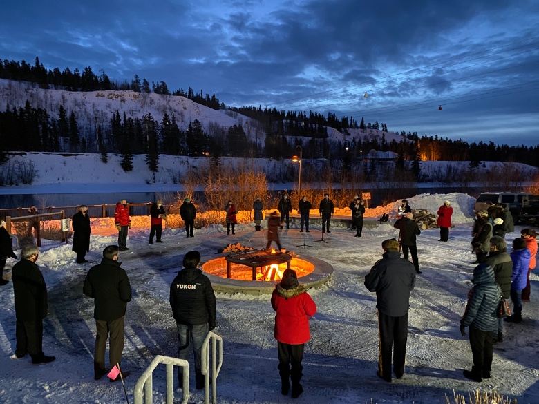 A group of people stand outside in a circle around a sacred fire.