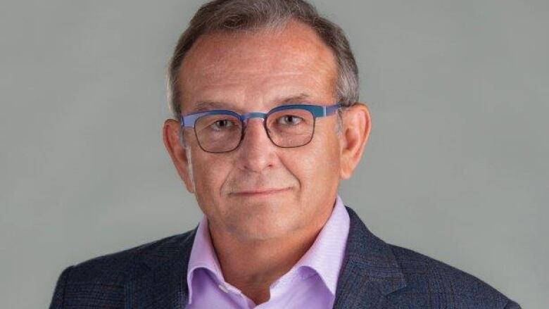 A man in a black blazer and purple shirt poses for a photo.