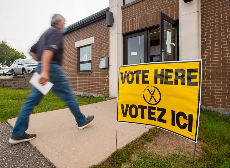 A man walking into a building with yellow Vote Here signs