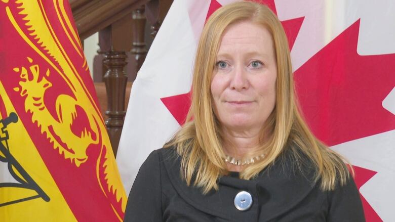 A woman stands in front of a New Brunswick flag, left, and a Canadian flag.