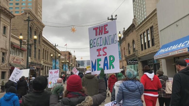 People holding signs and marching at a protest on a downtown street.