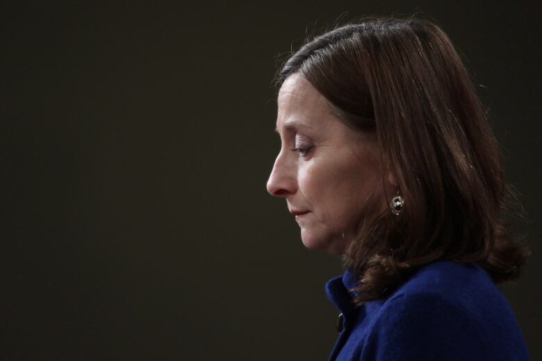 A side portrait of a woman, looking down. Black background.