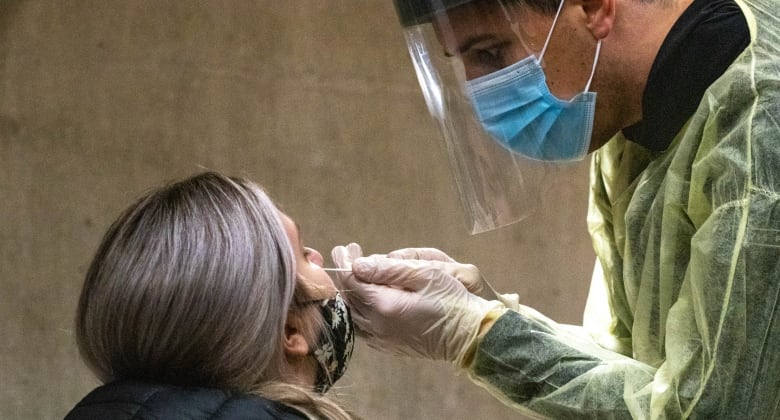 A woman tilts her head back as a male health-care worker wearing full protective gear inserts a long swab in her nostril. 