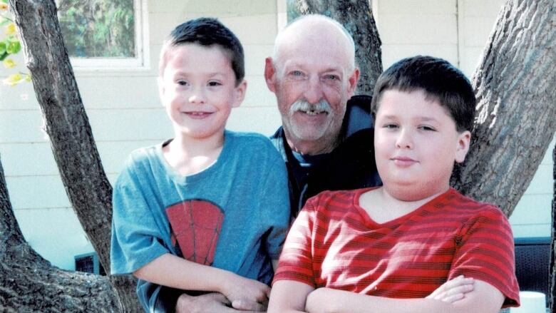 two young boys with an older man, their father sitting in a tree.