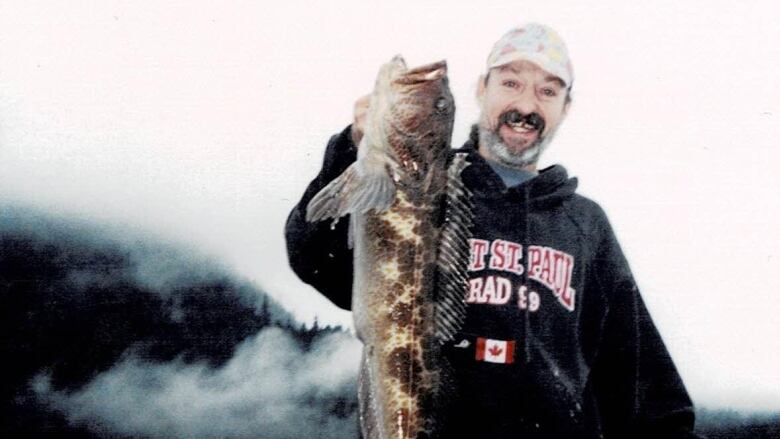 Man stands smiling at the camera, holding a fish that extends past his torso.