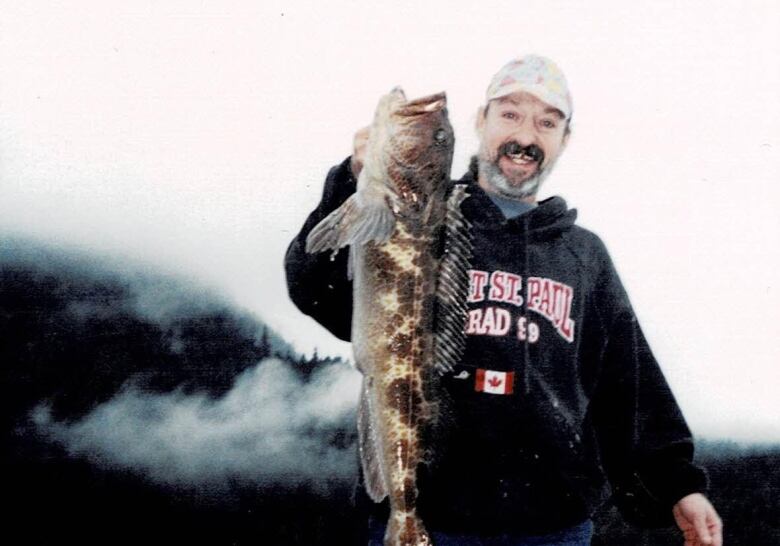 Man stands smiling at the camera, holding a fish that extends past his torso.