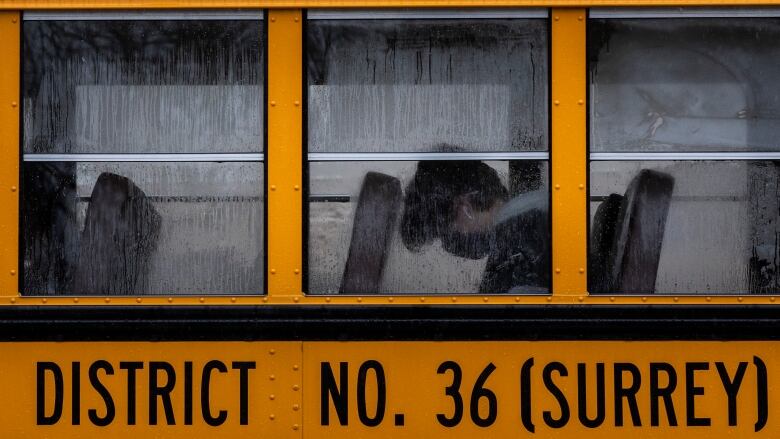 A boy in a mask sits in a school bus marked 'District no. 36 (Surrey)'.