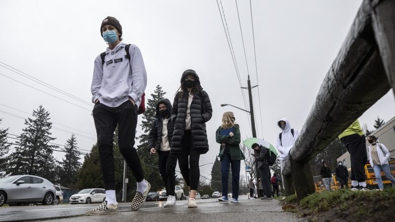 Students wearing masks walk in the rain outside Earl Marriott Secondary School. 