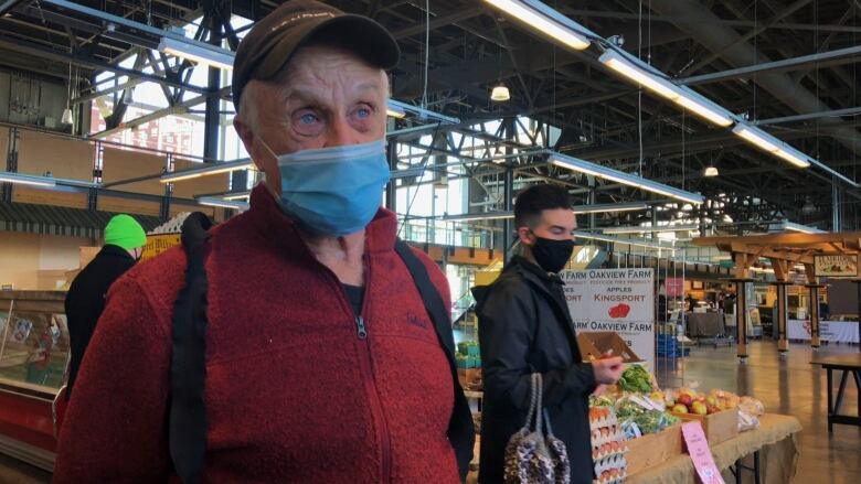 A man in a burgundy shirt and wearing stands in front of a produce stand.