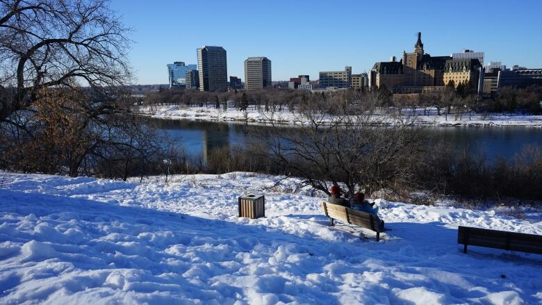 The skyline of a city is seen across a snowy park and a river.