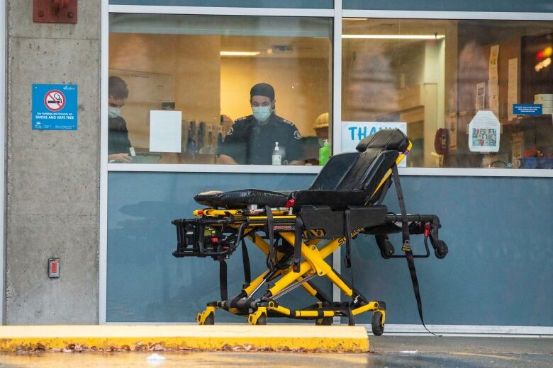 A man in black work attire is behind a window, with a stretcher in front of him.