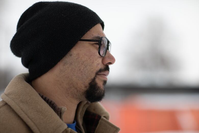 Man looking forward during the winter. He is wearing a black hat, glasses and a jacket. 