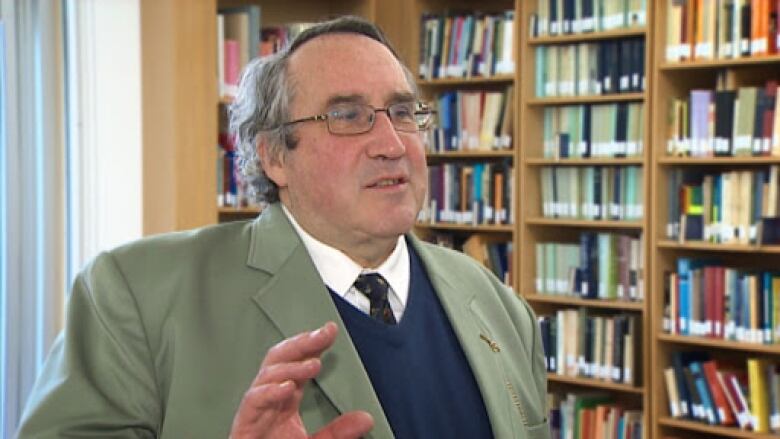 A man in a suit stands in front of shelves full of books.