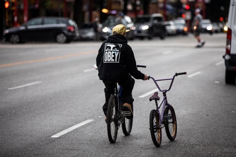 A man holds a small bicycle while riding down a street in Vancouver, British Columbia on Wednesday, August 26, 2020. 