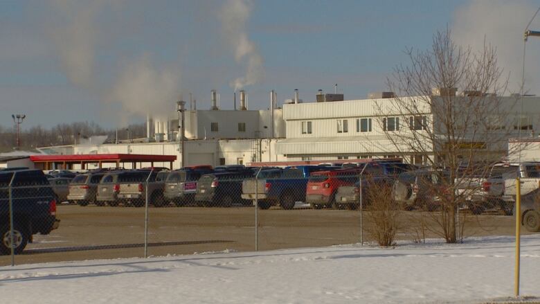 a white warehouse building with vehicles parked outside behind a wired fence. 