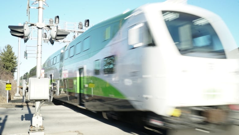 A GO Train speeds into a station on a sunny day. It is viewed from the edge of the platform.