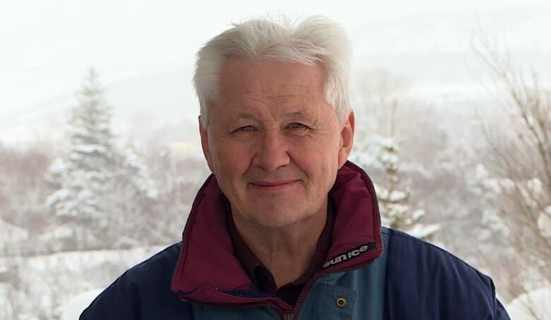 A man with white hair and a navy blue coat with red colour is looking into the camera.