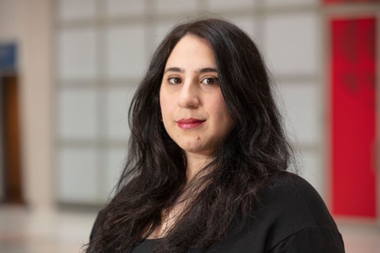 A woman with long dark hair looks at the camera.