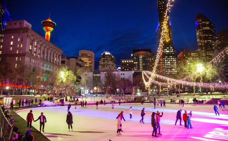 Skaters enjoy an outdoor ice rink under the lights at night surrounded by downtown towers.