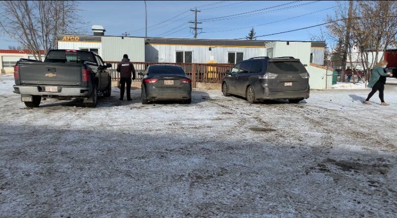 A mobile trailer in a parking lot with three cars and two people. 