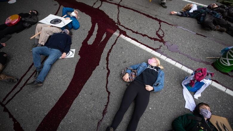 People lie on the ground while taking part in a die-in after members of Extinction Rebellion spilled red liquid representing blood on the street outside B.C. Supreme Court as part of a theatrical demonstration of mourning, during a protest to call for government action to address the climate and ecological crisis, in Vancouver, on Saturday, February 27, 2021.