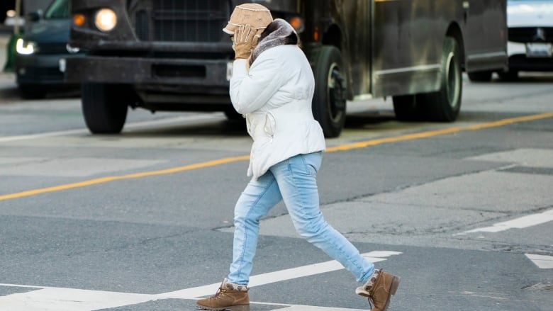 A woman holds onto her hat as she crosses an intersection near Toronto's Front Street on Monday, March 1, 2021. Environment Canada issued a special weather statement Monday, warning of winds gusting up to 80 km/h could develop Monday afternoon. (Sam Nar/CBC)