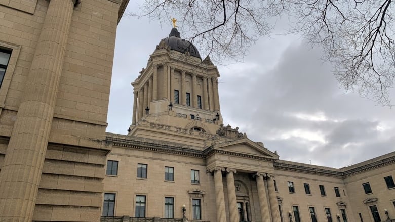 A grand stone building with pillars and a dome is seen under a cloudy sky.