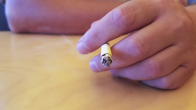 A close-up of a hand holding a burning cigarette.