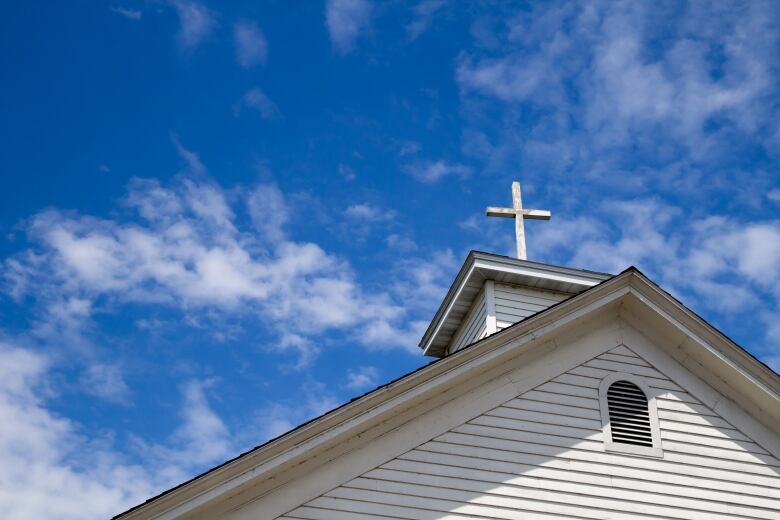 A wooden cross on a simple steeple set against a sunny summer blue sky.