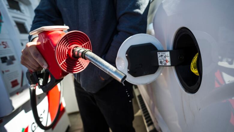 A man holds a leaking gas nozzle at a station while filling his car. 