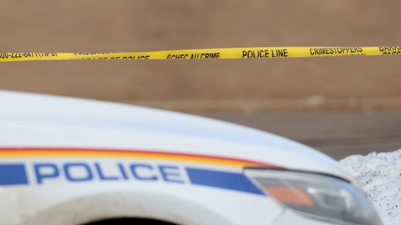 Yellow police tape stretches across the image with an RCMP cruiser in the foreground showing the work 