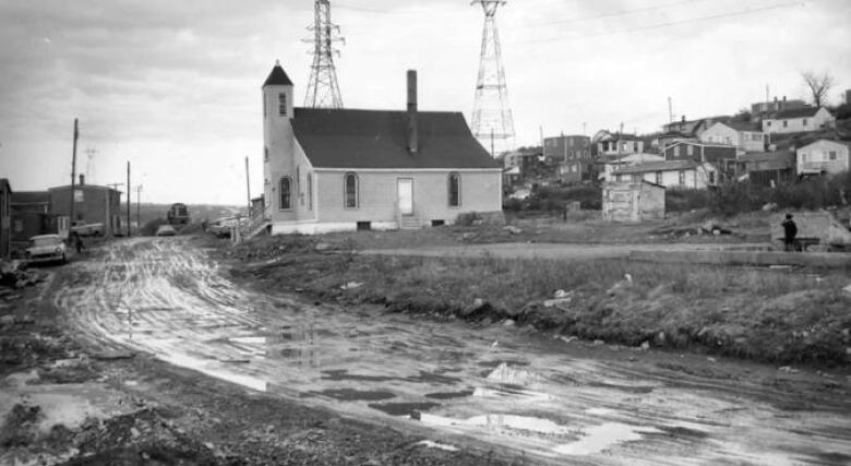 An old, black-and-white photo of a church, next to an unpaved, muddy road.