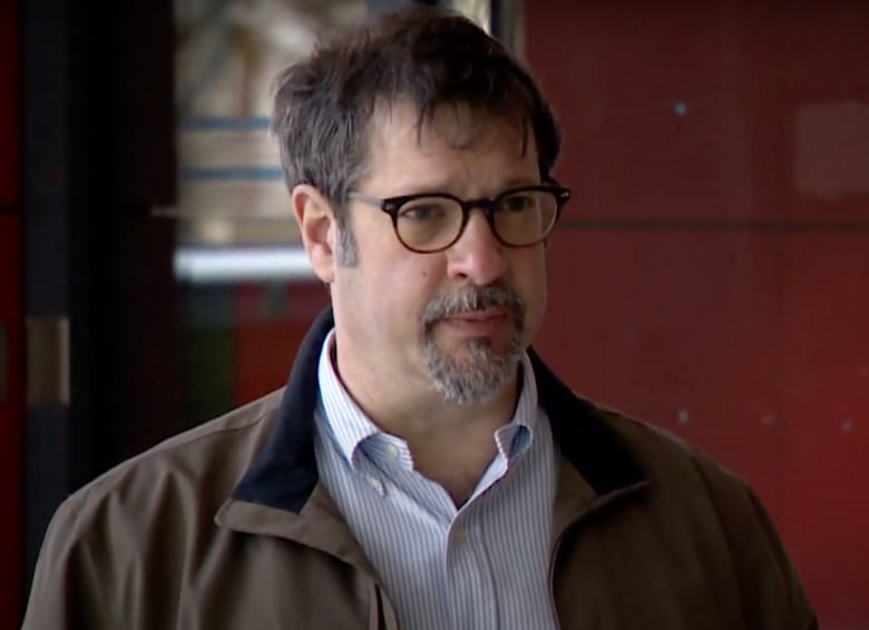 A man with a goatee and glasses speaks to a reporter.