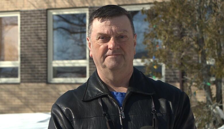 A man in a leather jacket stands in front of the Gander town hall.