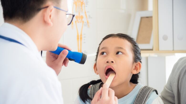 A doctor examining a young patient with a tongue depressor in the patient's mouth. 