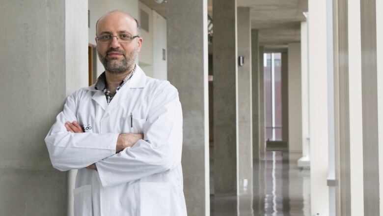 A man in a lab coat crosses his arms looking at the camera.