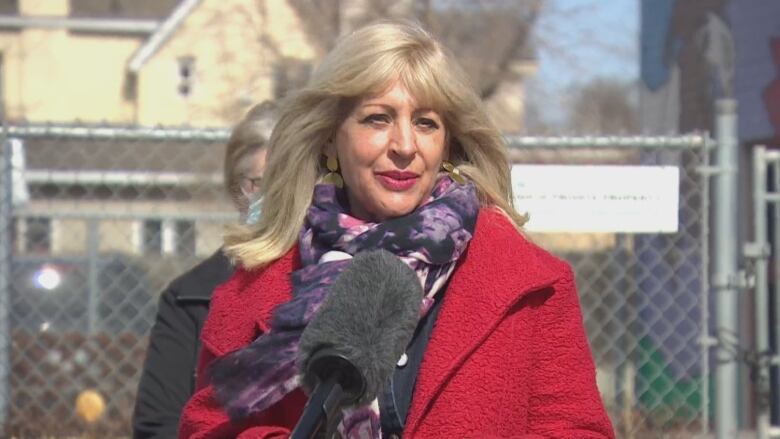 A woman in a red coat speaks at a podium outside.