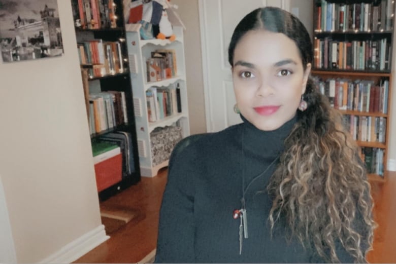 A woman with a black turtleneck and long curly hair smiles at the camera.