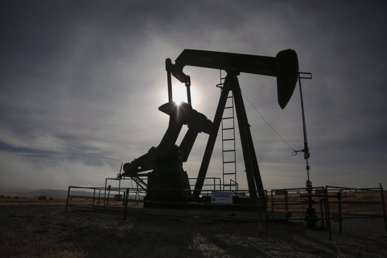 A pumpjack is seen in silhouette against the sun. 