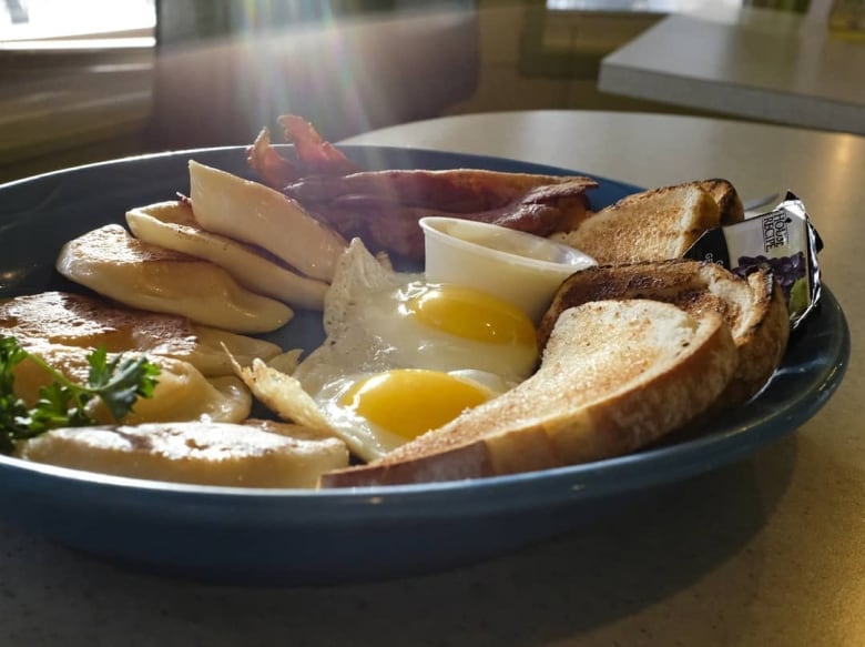 Bacon, eggs, toast and perogies are served on a breakfast plate.