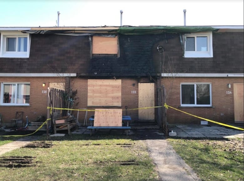 the middle townhouse in a row of three is charred from flames, has plywood over the windows and doors and police tape across the front of it