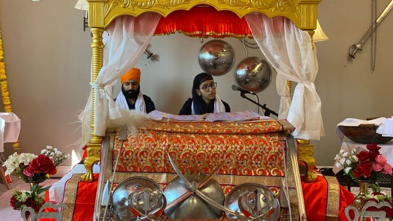 Two people read from a holy book inside a Sikh temple.