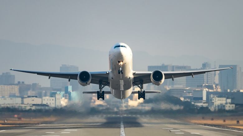 A commercial jet airplane is shown as it lifts off a runway. A cityscape can be seen in the background.